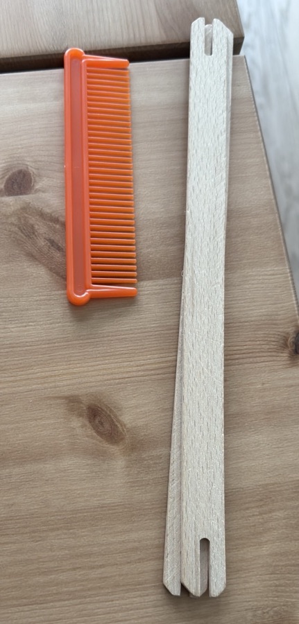 The orange plastic comb and the flat wooden shuttle with a notch at each end