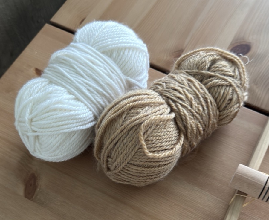 A ball of white wool and a ball of tan wool next to the loom